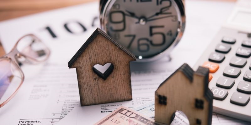 wooden houses on desk with paper, calculator, and money