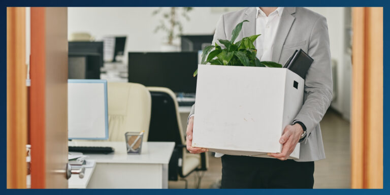 A man carrying a box of personal items from his desk while leaving the office.