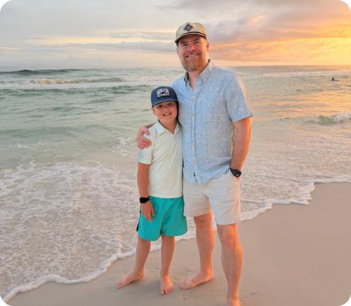 Father and son stand together on the beach at sunset, enjoying a moment by the water.