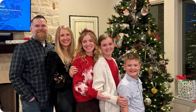 A family of five poses together in festive attire beside a beautifully decorated Christmas tree.