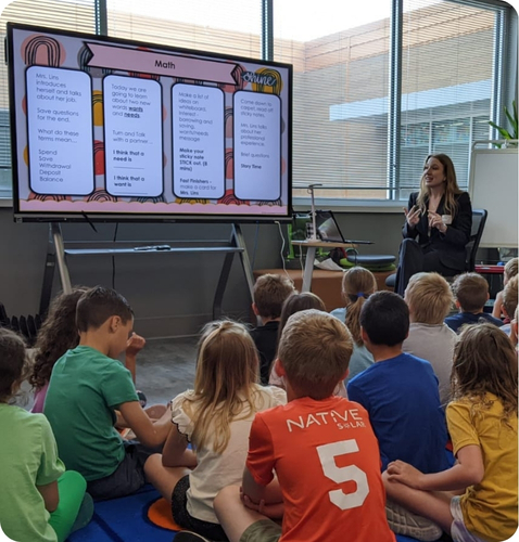 Alison Miller engages a group of children in a math lesson, discussing interactive activities displayed on a large screen.