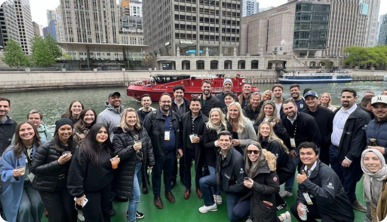 Group of professionals enjoying a networking event on a boat in Chicago, with city skyline and river in the background.