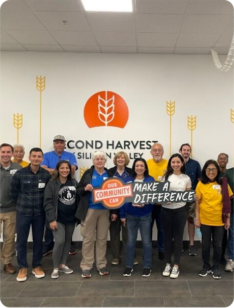 Community volunteers gather at Second Harvest of Silicon Valley, holding signs promoting local impact and support.
