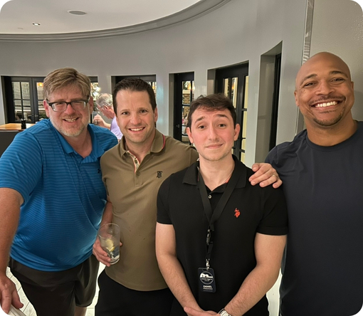 Four men pose together, smiling, in a social setting, showcasing camaraderie and friendship.