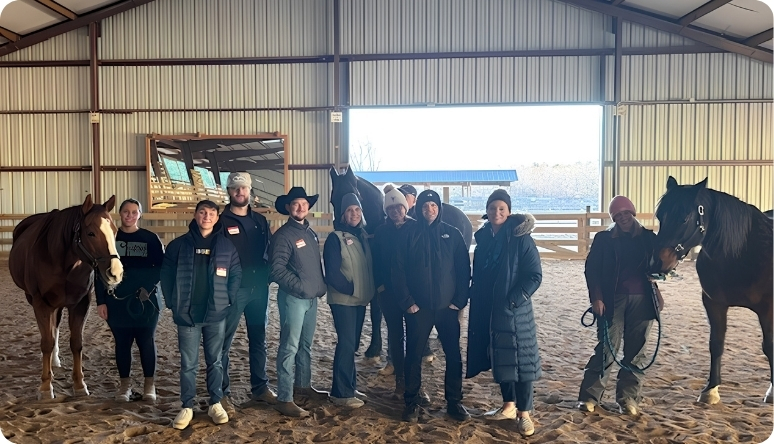 Group of people with two horses in a riding arena, engaged in a horse training or therapy session.