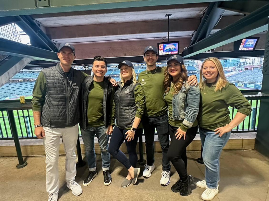 Matt Adams poses with Mission Wealth colleagues during a team outing at a baseball stadium.