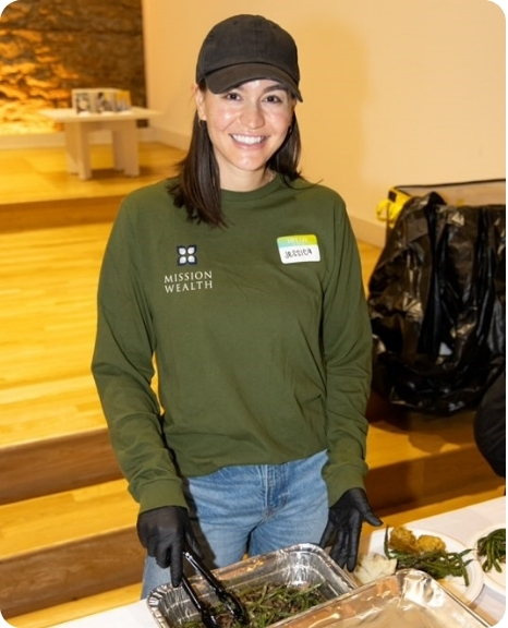 Jessica Mora, wearing a green Mission Wealth shirt and gloves, serves food at a community event.