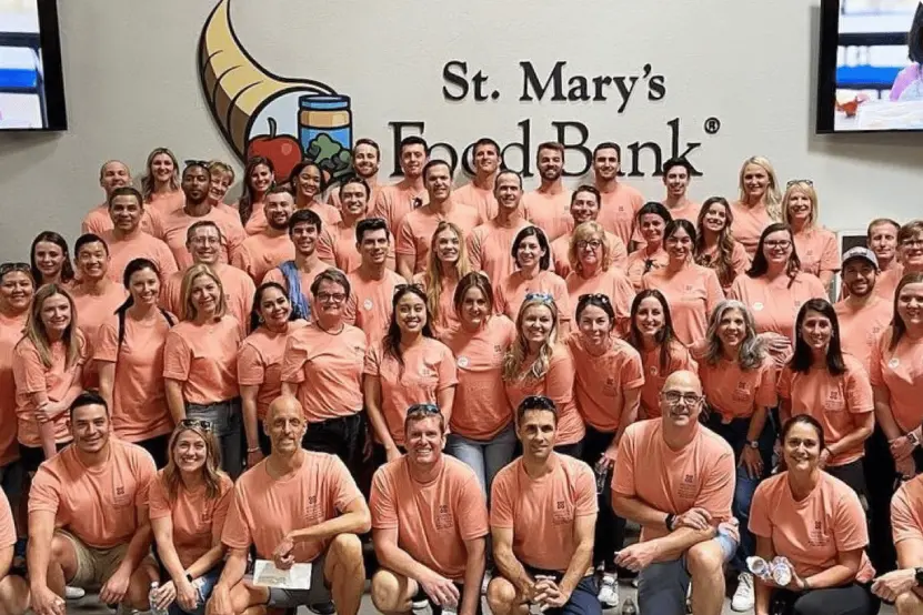 A large group of volunteers in matching orange shirts poses together at St. Mary's Food Bank.