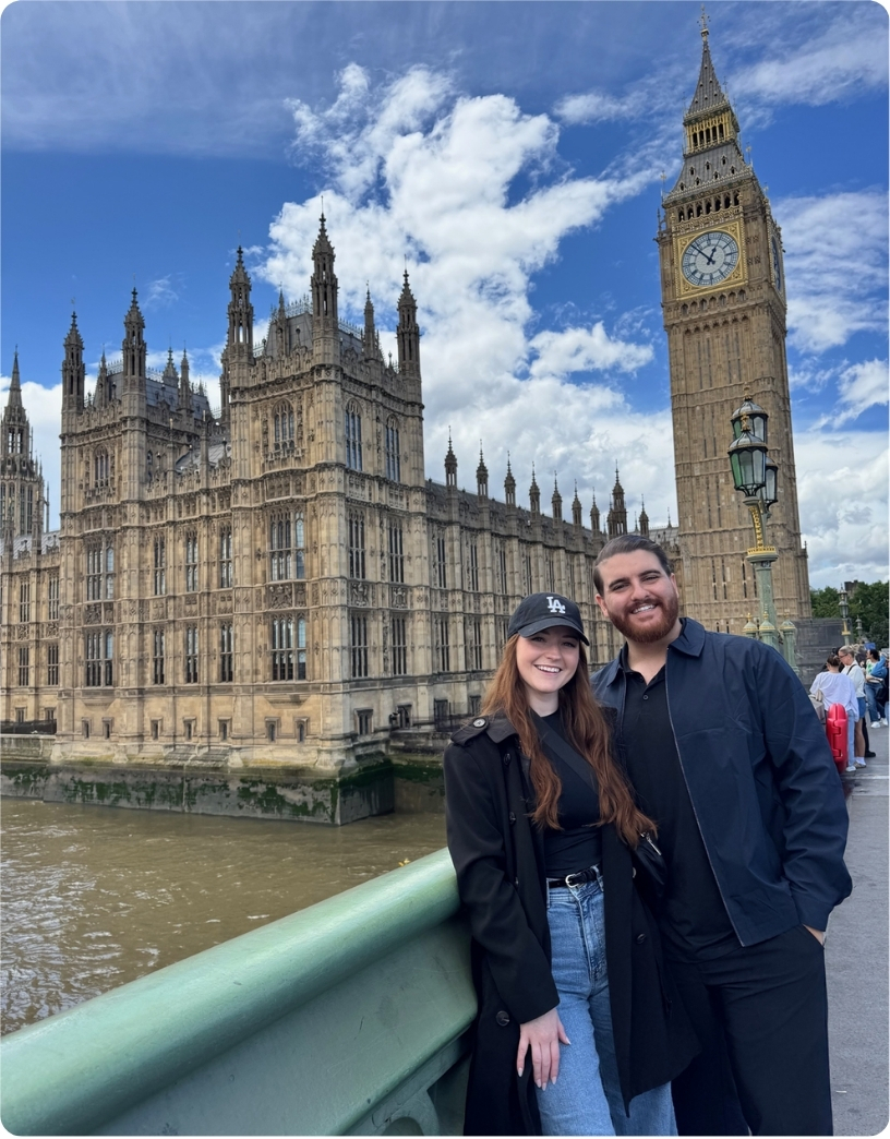 A couple poses in front of the Houses of Parliament and Big Ben on a sunny day in London.
