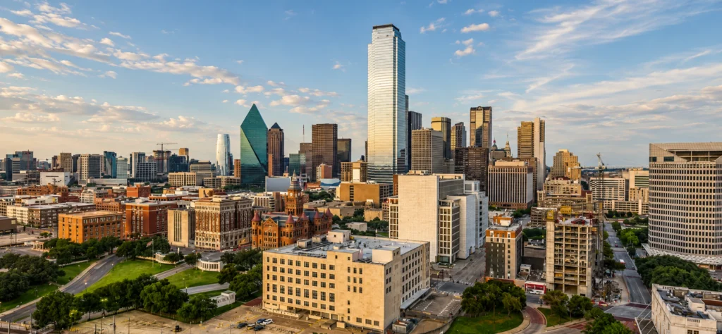 Dallas skyline featuring modern skyscrapers and historic buildings under a blue sky with scattered clouds.