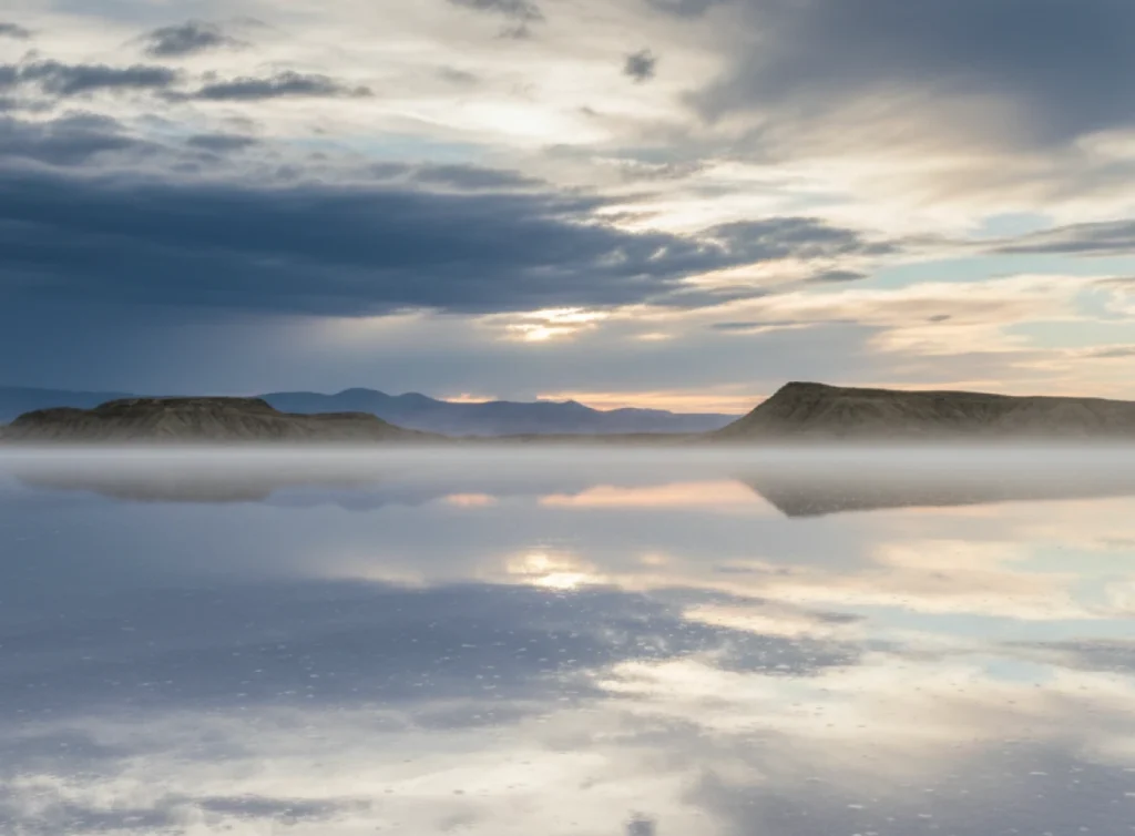 Serene landscape featuring misty reflections on a calm lake beneath a dramatic sky, highlighting the tranquility of nature.