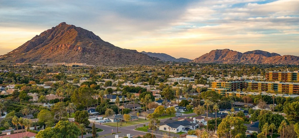 Scenic view of Scottsdale showcasing mountains, residential areas, and vibrant greenery under a colorful sky at sunset.
