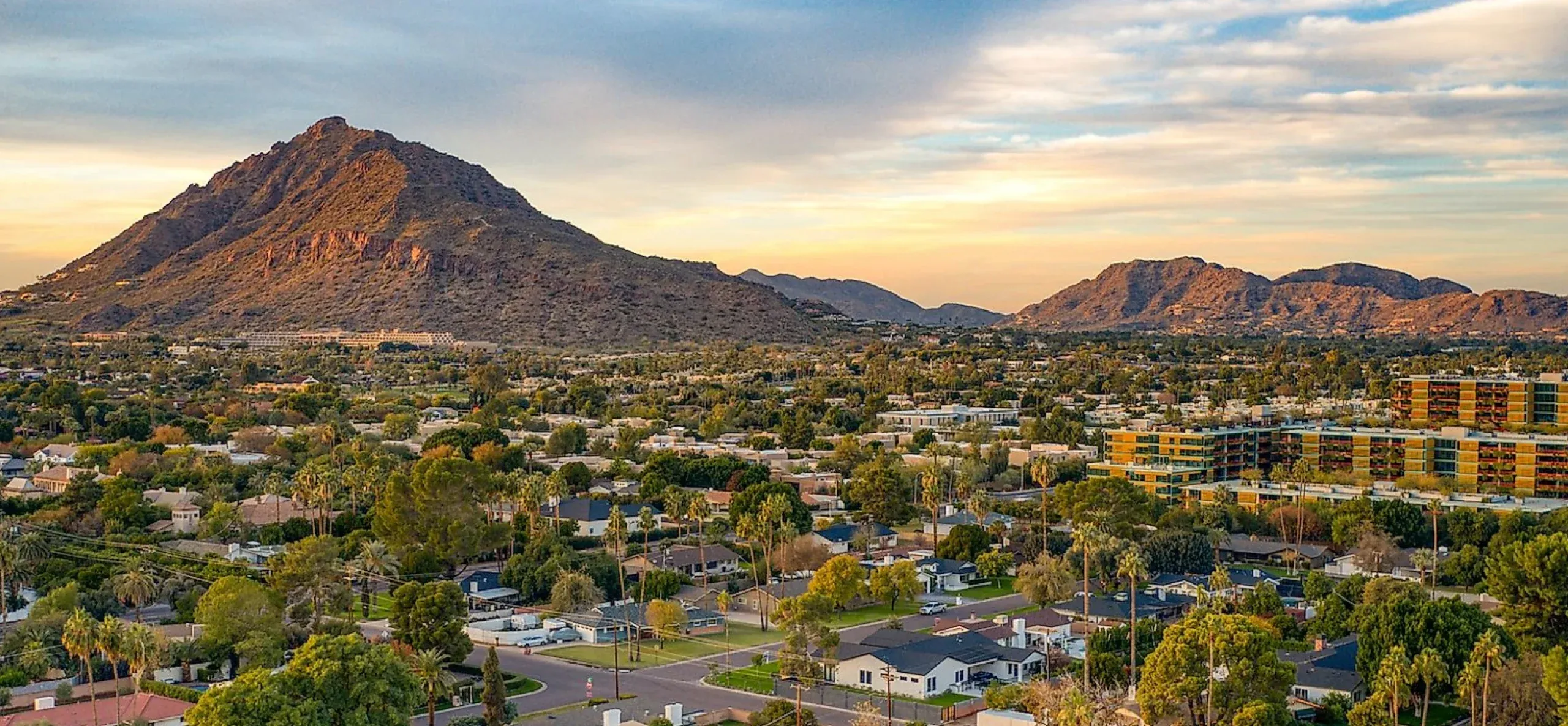 Scenic view of Scottsdale showcasing mountains, residential areas, and vibrant greenery under a colorful sky at sunset.