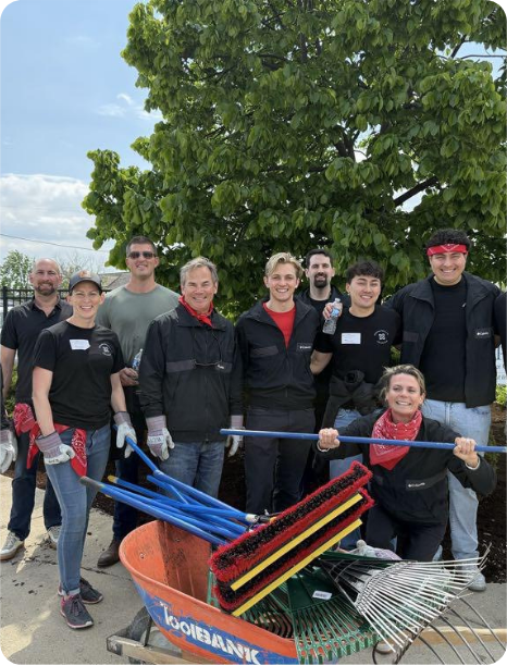 A group of volunteers poses with gardening tools, smiling after a community service project outdoors.