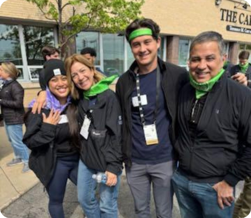 Four smiling individuals in matching outfits and green accessories pose together outside a building during an event.