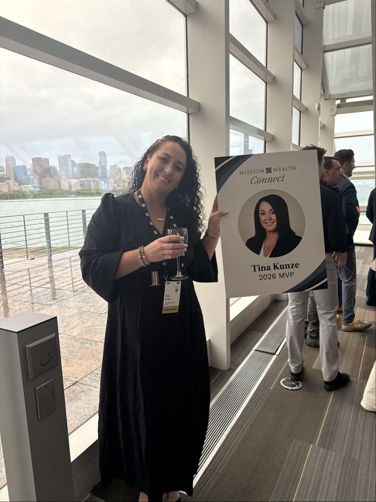 Tina Kunze poses beside her 2026 MVP recognition sign at Mission Wealth Connect.