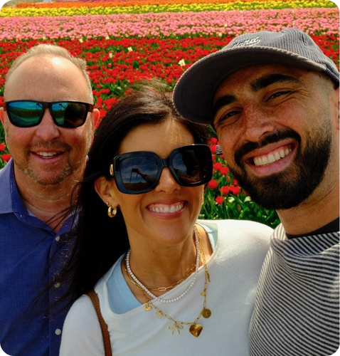 Three friends smiling in front of a vibrant tulip field, enjoying a sunny day outdoors.