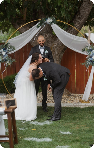 A couple shares a joyful moment during their outdoor wedding ceremony, framed by floral decorations and an arch.