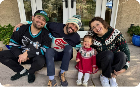 A family of four smiles together on a porch, wearing festive clothing, capturing a joyful moment.