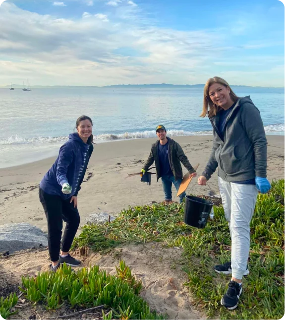 Volunteers from the Mission Wealth community impact participate in a beach cleanup, smiling while collecting debris.