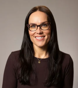 Professional headshot of Rachel Roberts, featuring her smiling with long dark hair and glasses against a neutral background.