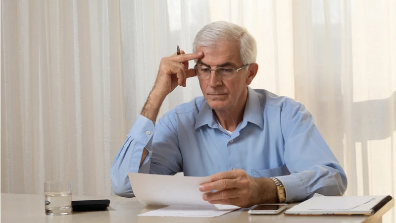 A senior man reviews financial documents with a thoughtful expression, highlighting the tension between financial theory and practice.