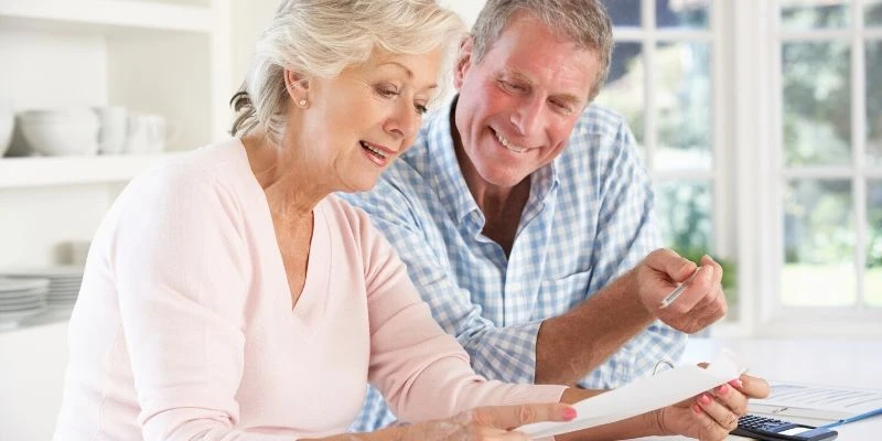 A smiling older couple reviews documents together, discussing options for starting a business after retirement.