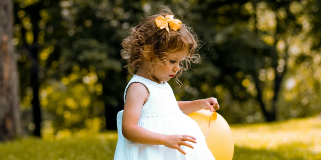 Young girl in a white dress holds a yellow balloon, symbolizing innocence and the importance of early financial education.