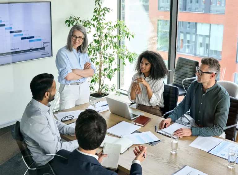 A diverse team collaborates in a bright conference room, discussing project milestones with a laptop and documents on the table.