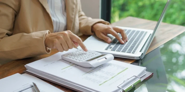 Calculating figures related to the Alternative Minimum Tax (AMT) using a calculator and laptop on a desk.