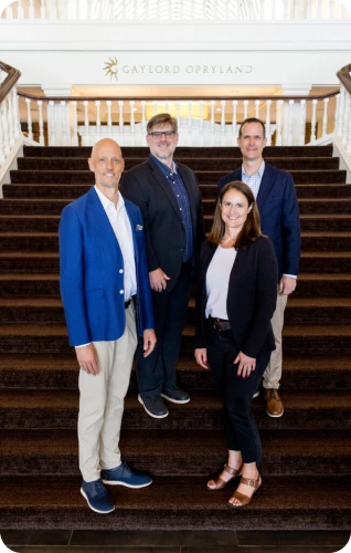 Four professionals pose on the staircase of Gaylord Opryland, showcasing a collaborative and welcoming atmosphere.