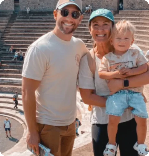 A family poses together at an ancient amphitheater, smiling joyfully while holding a young child.
