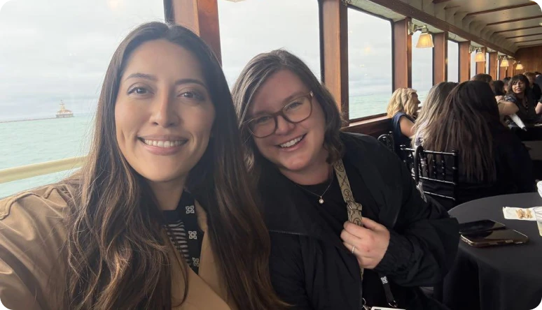 Two women smile for a selfie inside a boat, with a view of the lake and other guests in the background.