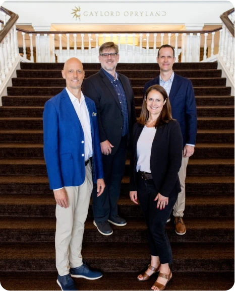 Four professionals pose on a staircase at Gaylord Opryland, showcasing a welcoming atmosphere for an event or meeting.