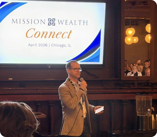 A speaker addresses an audience at the Mission Wealth Connect event in Chicago, April 2026, with a presentation screen behind.