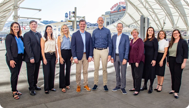 A diverse group of professionals poses together outdoors near a landmark, showcasing teamwork and collaboration.