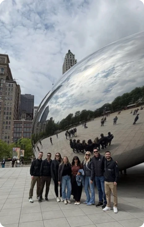 Group of seven friends pose in front of the reflective Cloud Gate sculpture in Chicago's Millennium Park.