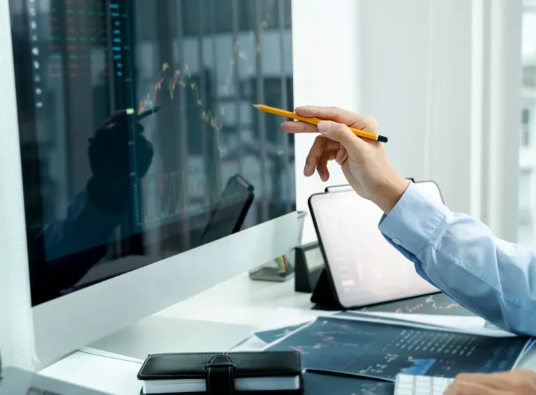 A person analyzes financial data on a computer screen while taking notes with a pencil.