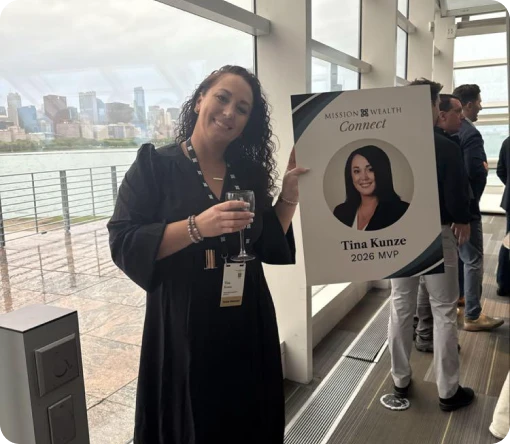 Tina Kunze, holding a drink, poses with her MVP sign at a networking event by the waterfront in a city setting.