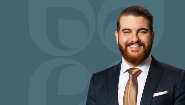 Smiling man in a suit with a tie stands against a blue background, conveying professionalism and approachability.