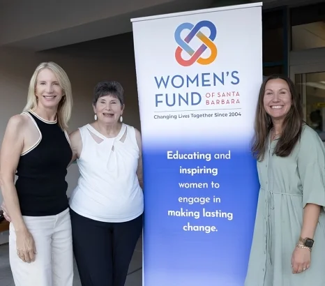 Three women standing beside a Women's Fund of Santa Barbara banner promoting education and empowerment for lasting change.