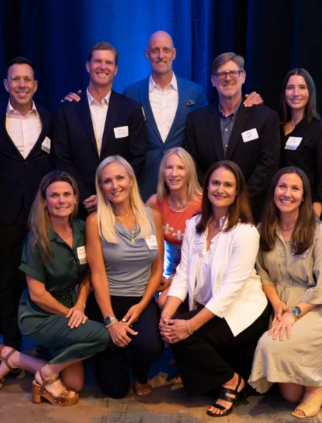 A diverse group of twelve professionals poses together at a formal event, smiling against a blue backdrop.