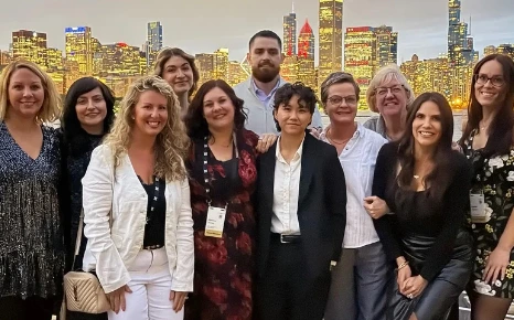 A diverse group of women and men poses together against a city skyline backdrop, showcasing camaraderie and celebration.