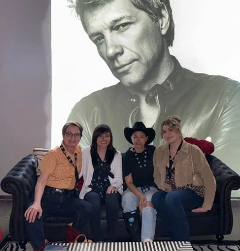 Four people sit on a couch in front of a large black-and-white portrait of a man, smiling and posing for the camera.