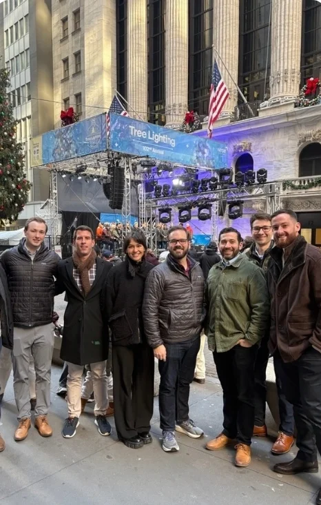 Group of friends posing in front of a tree lighting stage in a festive city setting during the holiday season.