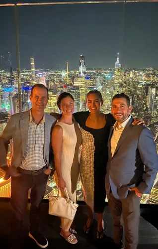 Four friends pose together at a rooftop venue with a stunning city skyline illuminated at night.